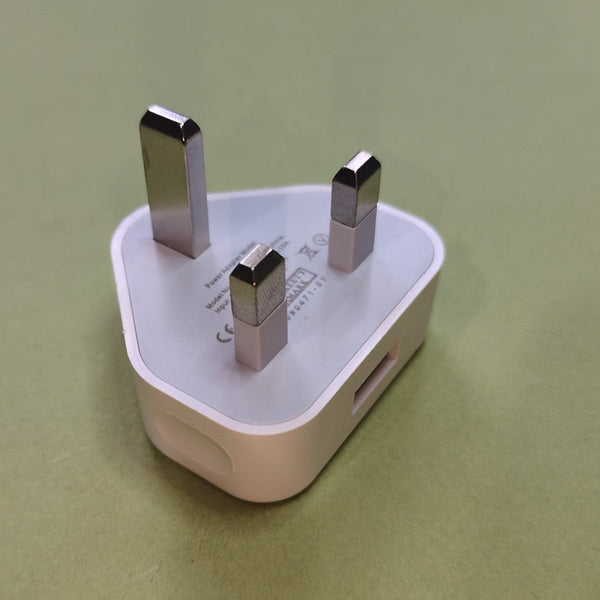 A white triangular UK three-pin wall charger plug with silver metal prongs, shown on a solid olive green background.
